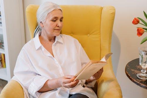 Free Senior woman enjoying a quiet reading moment in a cozy home with a warm atmosphere. Stock Photo