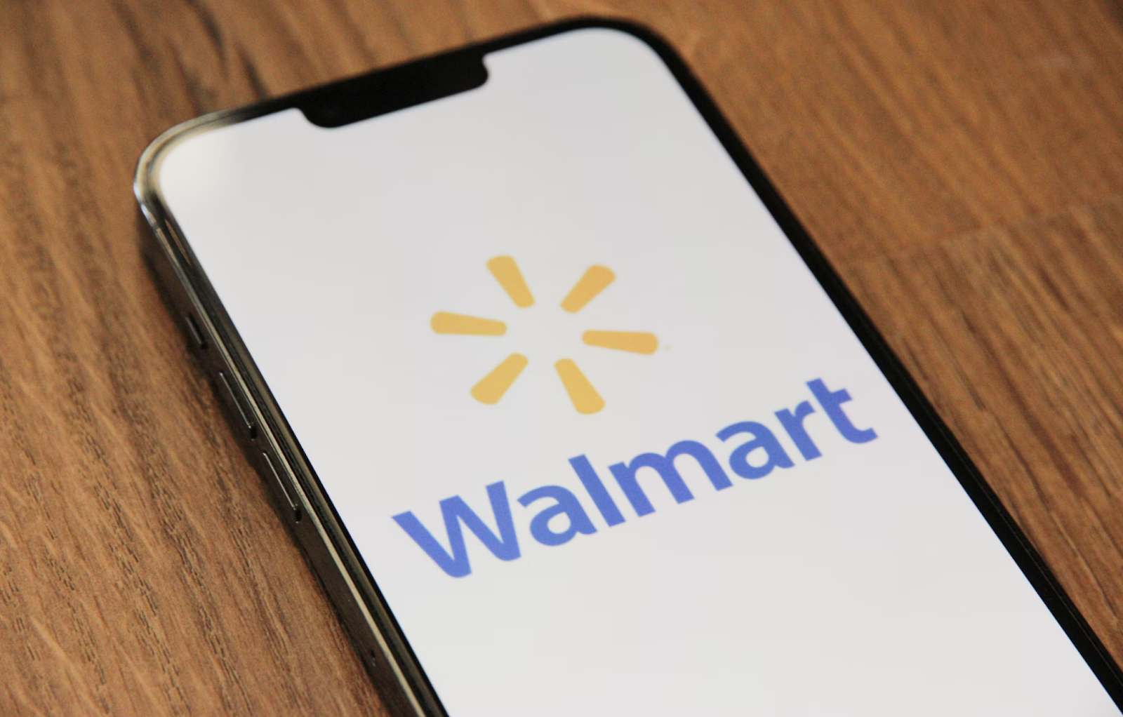 Walmart logo displayed on a smartphone screen placed on a wooden surface.